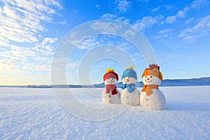 Friends snowman in red, blue, yellow hats and scarfs. Nice winter scenery with mountains, field in snow. Orange sunset background.