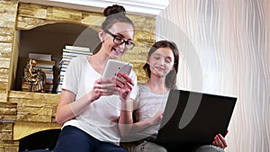 Friends socializing at home and playing games on laptop and tablet, girls sitting together