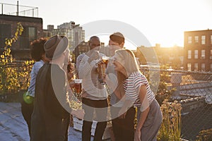 Friends stand talking at rooftop party, backlit by sunlight