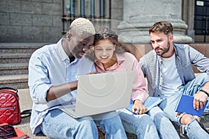 friends are students using a laptop while sitting on the steps.