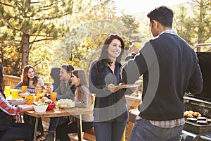 Friends at a table and two talking by grill at a barbecue