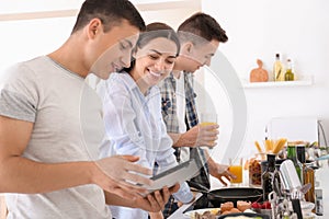 Friends with tablet PC reading recipes in kitchen