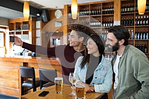 Friends taking selfie with mobile phone while having glass of beer