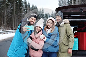 Friends taking selfie near open car trunk on road.