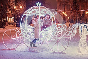 Friends taking selfie photo in illuminated fairy tale carriage with horses decorated with lights and garlands for Christmas