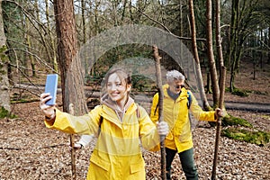 Friends taking selfies during forest hiking in raincoats with backpacks. Trekking travel in adventure lifestyle, nature