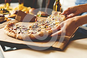 Friends taking slices of tasty pizza from plate, close up view.