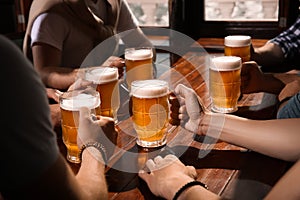 Friends with tasty beer at wooden table in pub, closeup