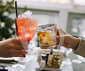 Friends toasting with glasses of whiskey and strawberry cocktail