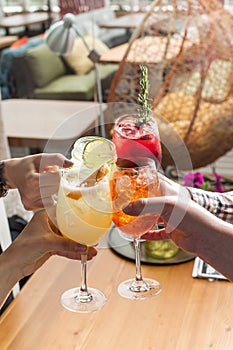 Friends toasting saying cheers hands holding summer cold cocktail drinks on cafe background