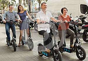 Friends of tourists of different generations enjoy a ride on electric scooters