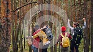 Friends tourists are raising hands and laughing standing on top of mountain then hugging each other congratulating on