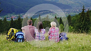 Friends of tourists sit in a picturesque place in the background of the mountains. They rest, admire the beautiful