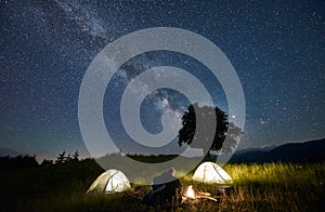 Friends travellers spending time in the mountains sitting around bonfire in camping under beautiful starry sky