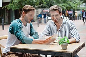 Friends using smart phone while sitting at sidewalk cafe