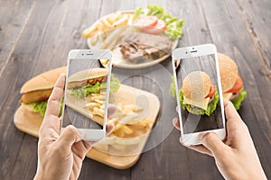 Friends using smartphones to take photos of hot dog and hamburger.