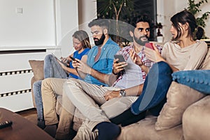 Friends using their mobile phones sitting on a sofa at home