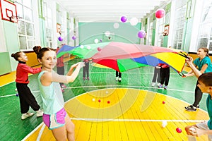 Friends waving parachute with balls in sports hall