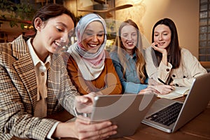 Friends. Women Meeting In Cafe. Group Of Four Smiling Girls Sitting In Restaurant With Laptop And Tablet. Diversity Female Working