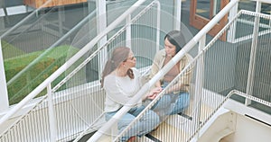 Friends, women sitting on stairs at apartment building and talking, sharing advice and support in life crisis. Trust