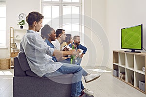 Friends young guys and girls are watching soccer football game on tv together sitting on couch.