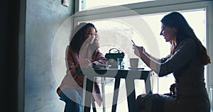 Friendship concept. Two happy beautiful multiethnic smiling female friends meeting at trendy coffee shop window table.