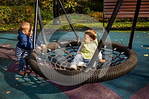 Friendship concept. two toddlers a boy and a girl play cheerfully and swing on a swing hammock on a playground in the