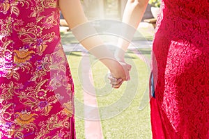 Friendship and lifestyle concepts. Two women wear cheongsam holding tight their hands while walking together on the garden