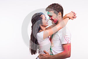Friendship, love, festival of holi, people concept - young couple playing with colors at the festival of holi on white