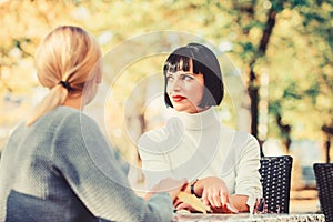 Friendship meeting. Friendship or rivalry. Girls friends drink coffee talk. Conversation of two women cafe terrace