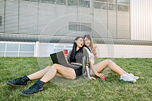 Friendship, summer vacations and urban lifestyle. Two smiling pretty asian girls sitting on the green grass on the big