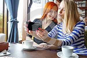 Friendship and technology. Two pretty girls using smartphones while drinking tea at cafe.