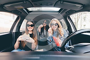 Friendship and time together on road. Three young and beauty women have fun together eating fast food and drive a car in road trip