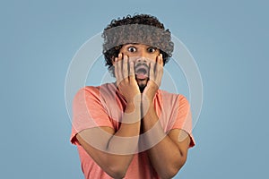 Frighten eastern guy touching his face, blue background