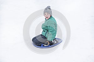 Frightened boy slides down the hill on snow saucer. Seasonal concept. Winter day