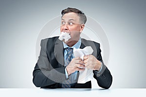 Frightened businessman in a dark jacket, shirt and tie eats paper on light grey background. The concept of document destruction