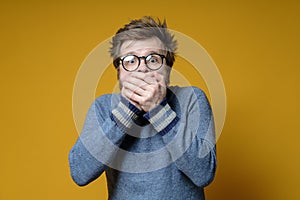 Frightened Caucasian man covers his mouth with hands and looks into the camera with big eyes.