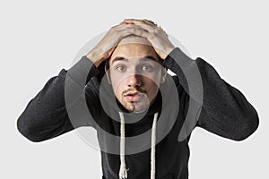 Frightened caucasian young man is looking into the camera with hands on his head. Mistake concept