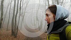 Frightened cautious girl traveler with a backpack cautiously goes through the misty autumn forest. A dangerous hike alone