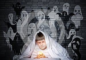 Frightened child with flashlight under blanket