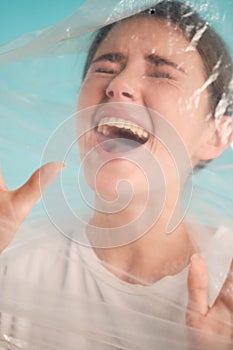 Frightened girl scaredly screaming in plastic bag over colorful background 