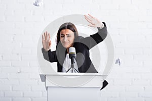 frightened lecturer suffering from glossophobia gesturing with hands while standing on podium tribune.