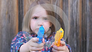 Frightened little blurred girl is holding in hands an orange and blue toy gun