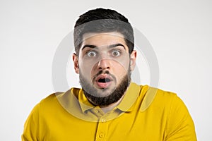 Frightened man afraid of something and looks into camera with big eyes full of horror over white wall background.