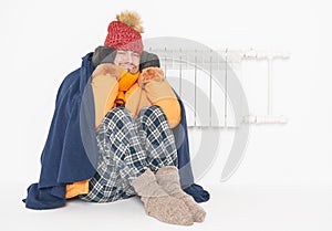 Frightened man feeling cold in hat and down jacket sitting close to radiator. Gas crisis concept