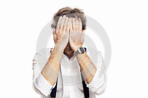 A frightened man in a white shirt and suspenders covered his face with his hands. White background. Economic crisis during the