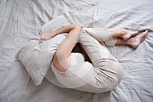 Frightened mature woman lying on bed fetal position covering pillow