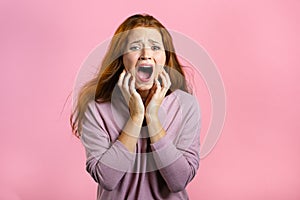 Frightened and screaming woman shocked isolated over pink background. Stressed and depressed pretty girl because of bad