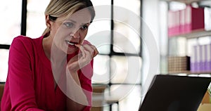 Frightened woman biting nails while working on laptop