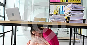 Frightened woman hiding under table in office